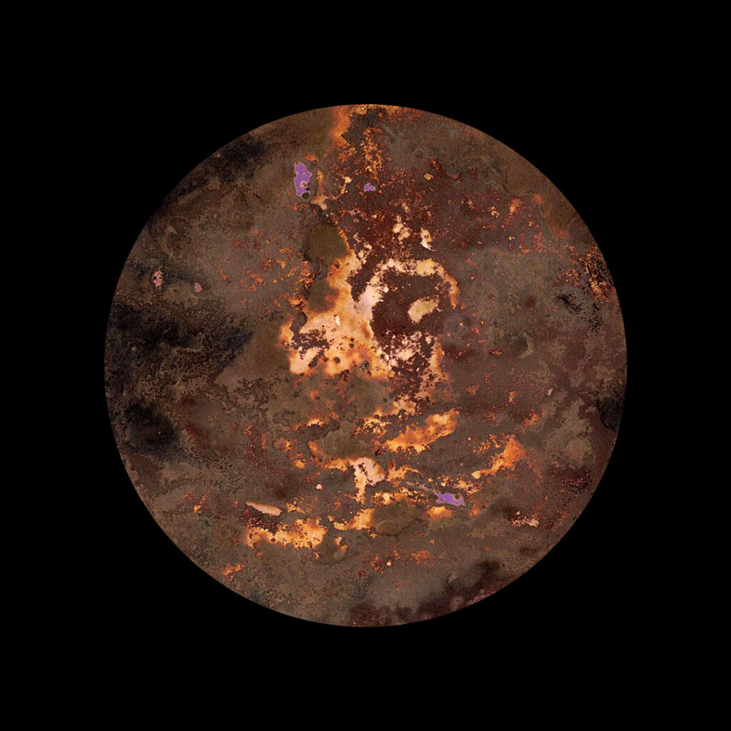 A lumen print which looks like a planet created from painting soil onto photographic paper. The print is dark and mid-brown, with elements of golden brown and splotches of pink